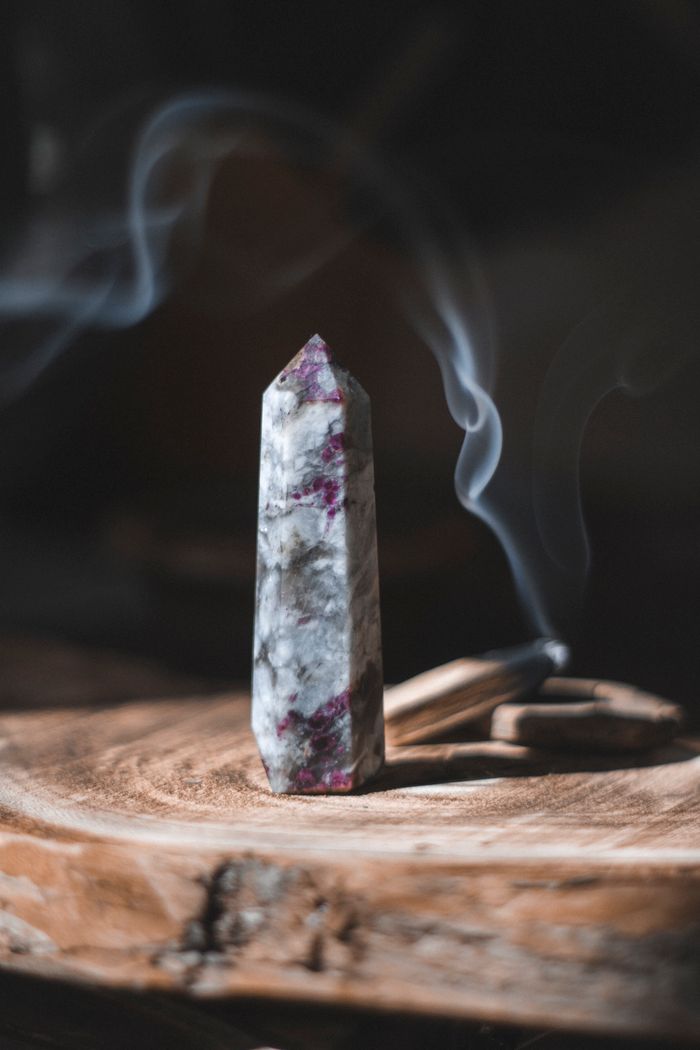 A smoky crystal mineral emits light smoke on a rustic wooden surface.